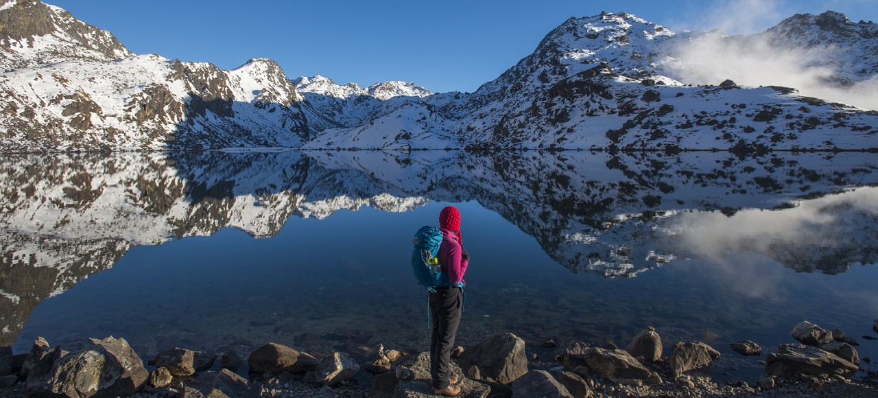 A lady in a purple hat and backpack gazing at the calm waters of Gosaikunda Lake, Nepal