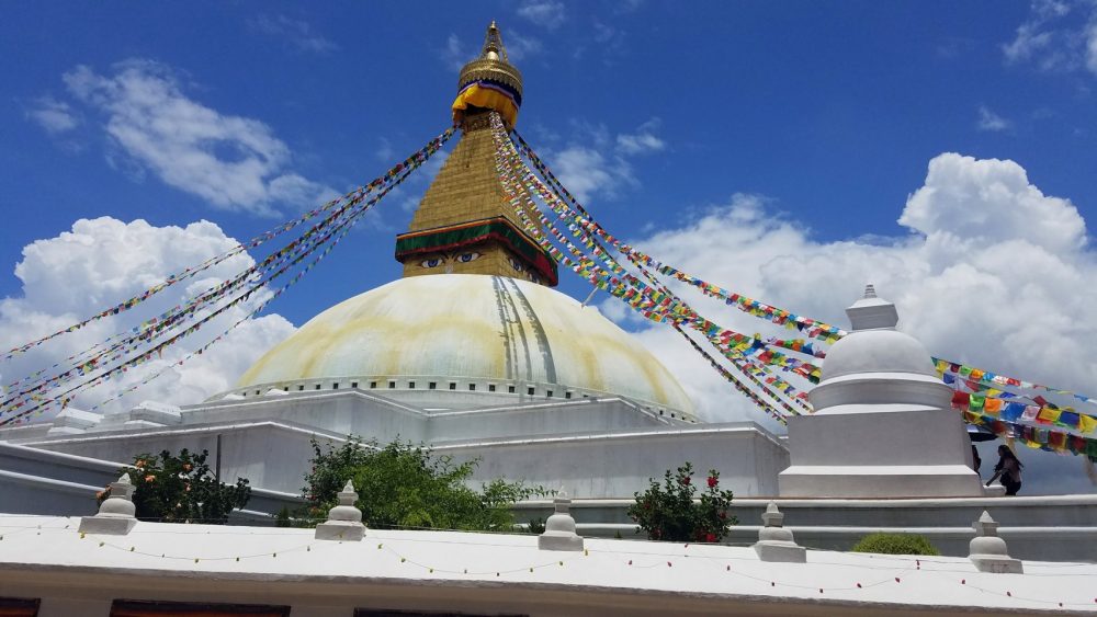 The Boudha Stupa with prayer flags framed against clouds and a brilliant blue sky